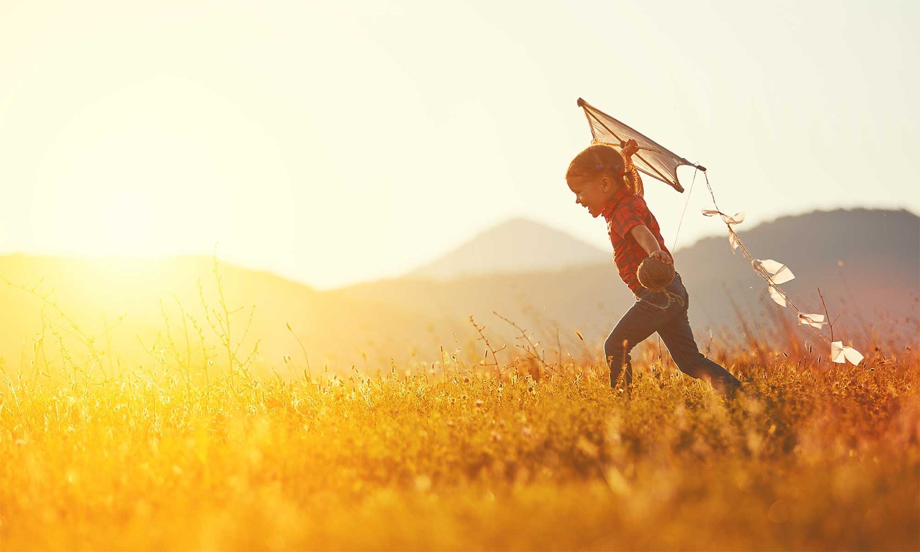 A child running through a sunlit field with a kite