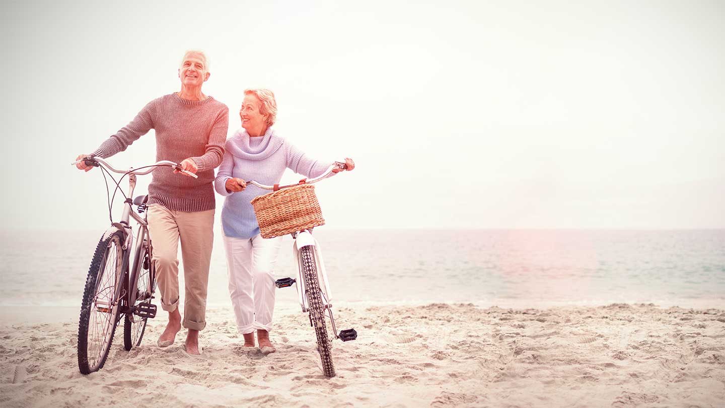 An older couple standing with bicycles on a beach
